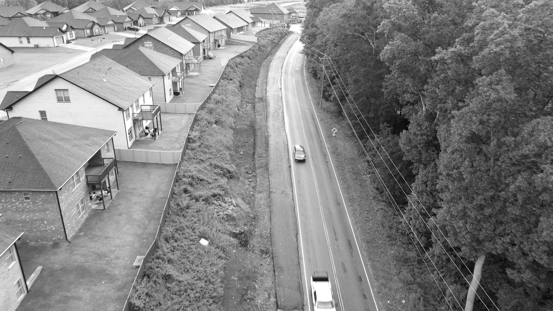 Aerial view along a Greenville County road Dillard Construction Group widened, with fresh asphalt on the new lane between a neighborhood and the trees.